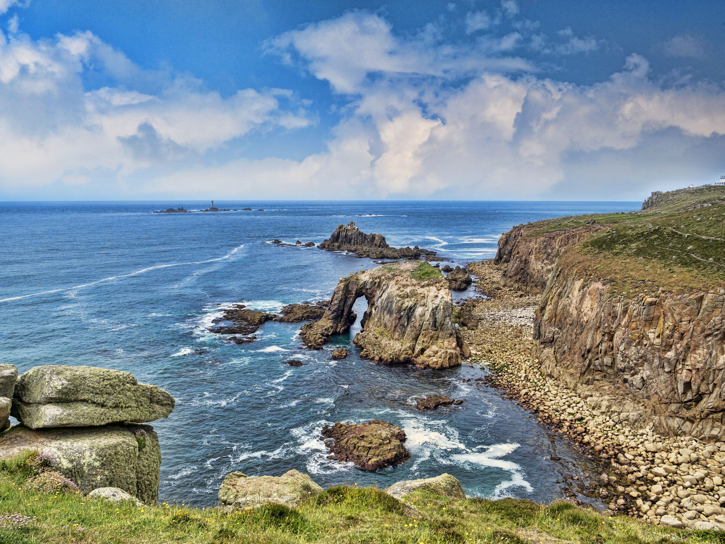 Rocky coastline of Lands End, Cornwall, UK, with the arch, Enys Dodnan, and the rock formation The Armed Knight, with the Longships Lighthouse offshore.