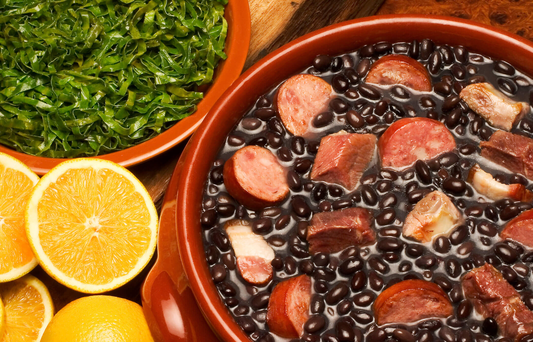 The stew of meat and beans sits in a red pot surrounded by lemons and a green garnish