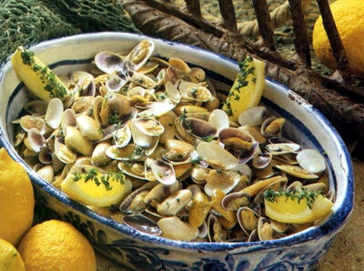A blue and white pot sits filled with seafood, lemons and herbs.